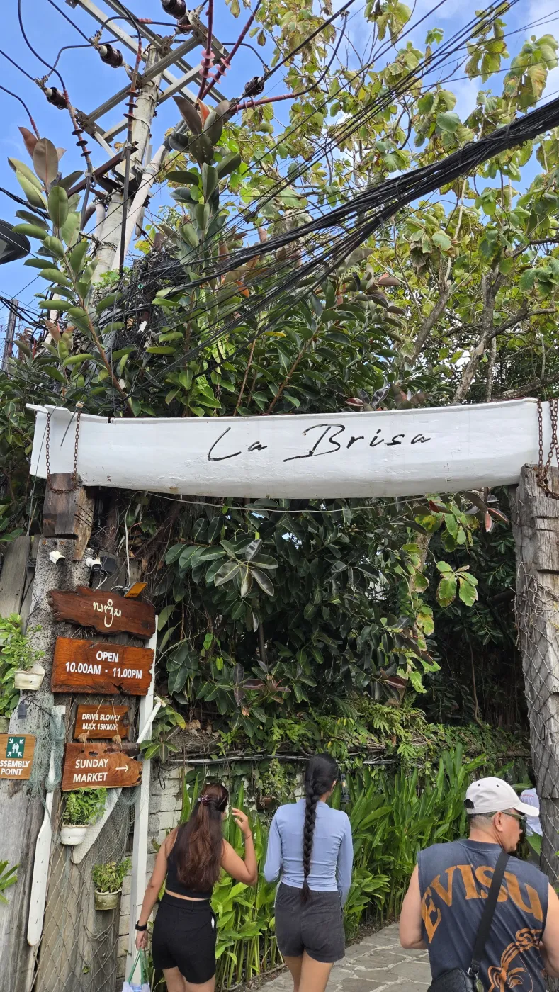 흰 배 모양 간판에 ‘La Brisa’라고 적힌 입구와 그 아래 SUNDAY MARKET 표지판