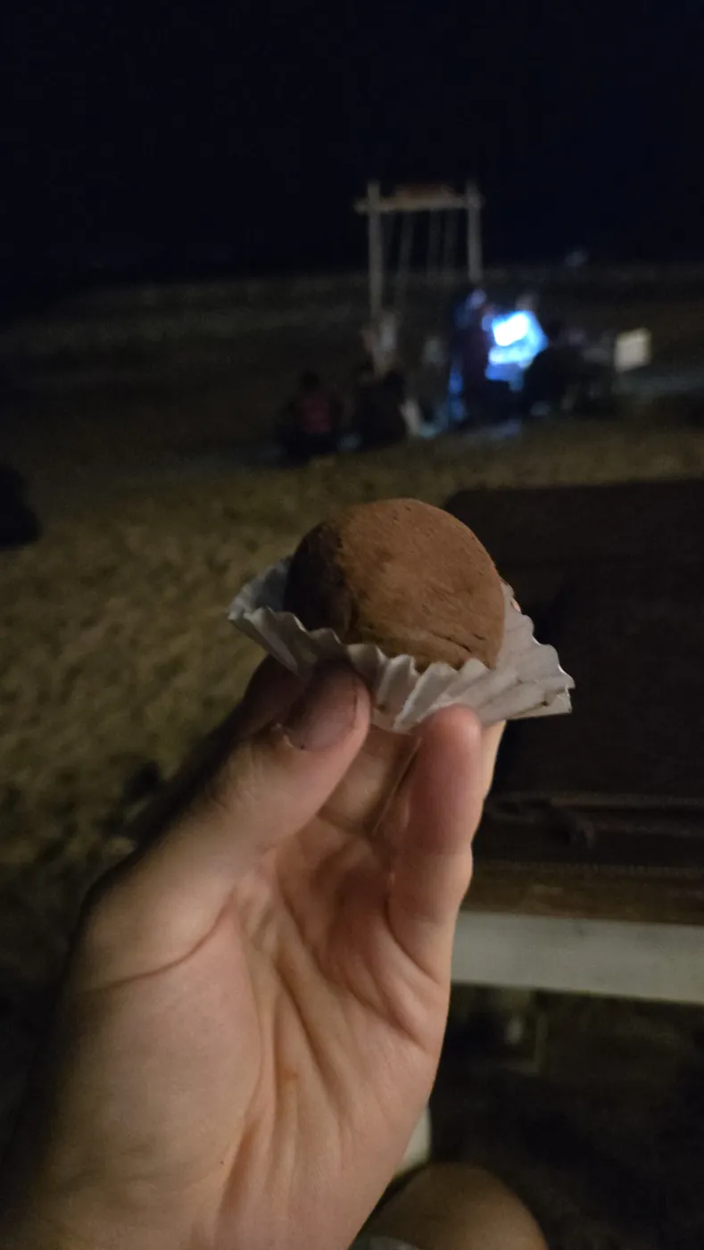 코코아 가루를 묻힌 두쫀쿠 한 알, 뒤로 밤바다와 파란 조명이 보인다