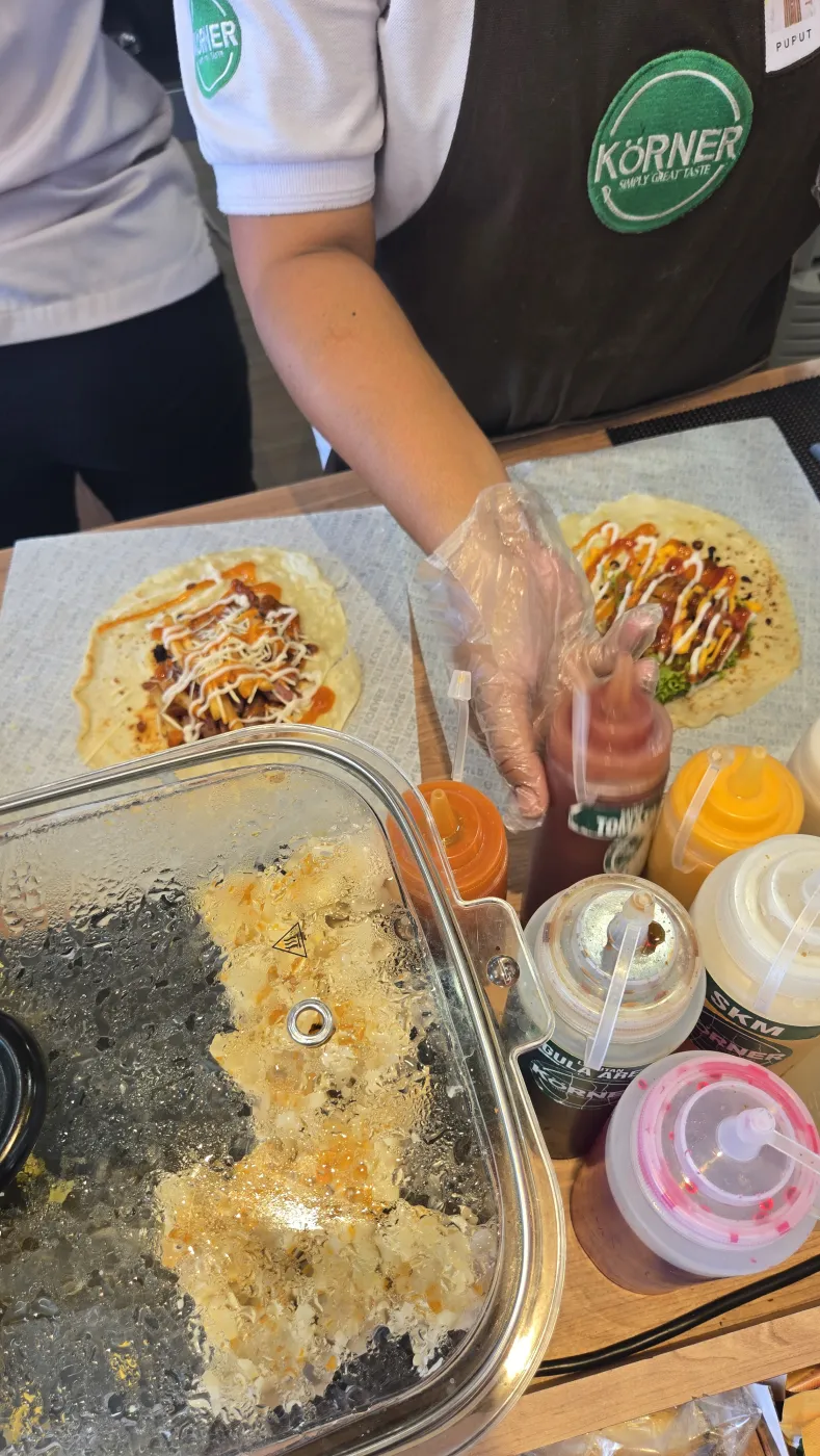 KÖRNER 좌판에서 또띠아에 소스를 뿌려 랩을 마는 직원과 소스 병들