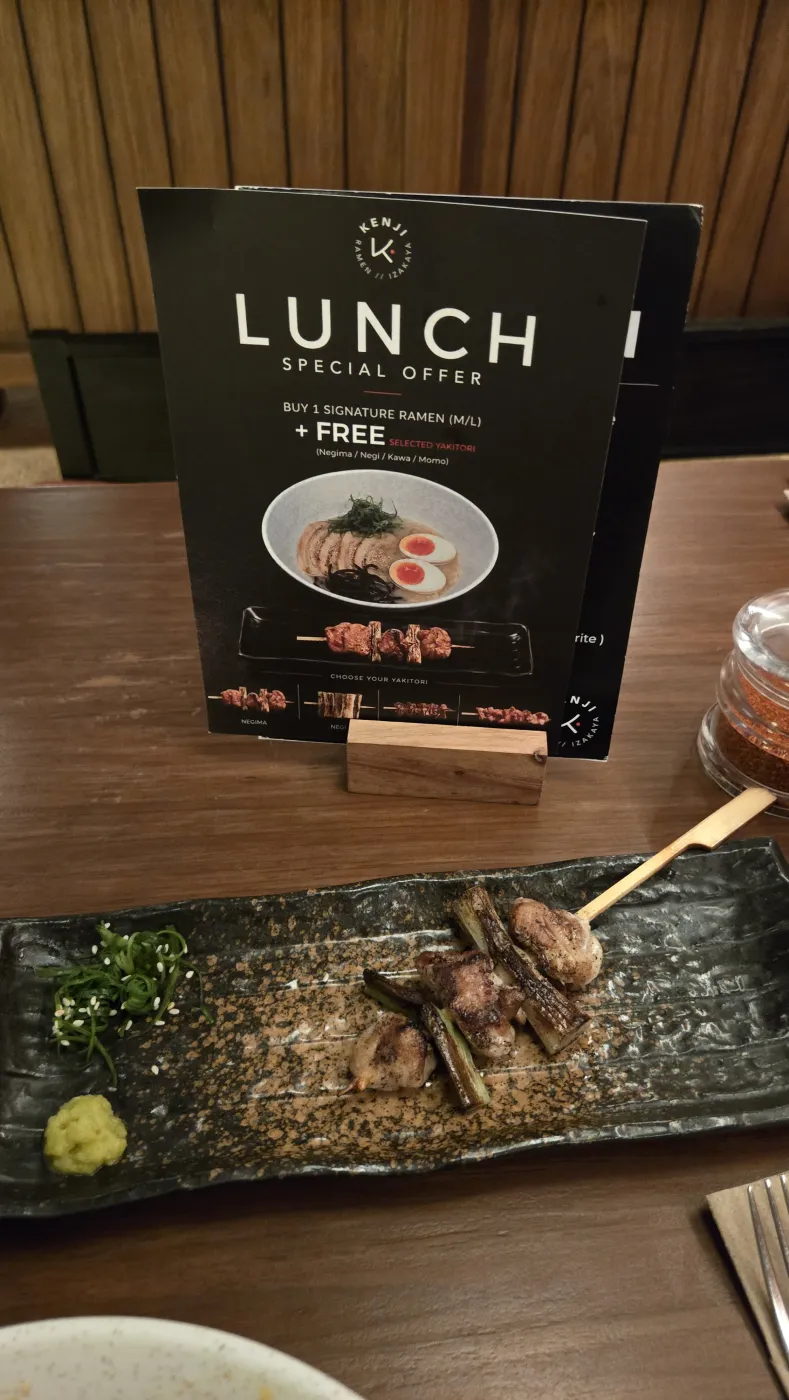 Kenji 라멘의 ‘라멘 주문시 야키토리 무료’ 런치 메뉴판과 검은 접시에 담긴 야키토리 꼬치