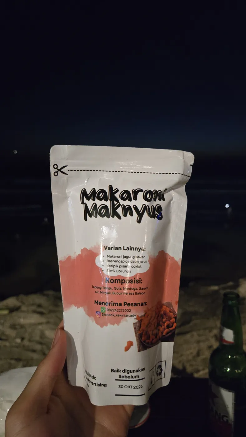 밤 해변에서 손에 든 ‘MAKARONI MAKNYUS’ 과자 봉지, 옆에 빈땅 병